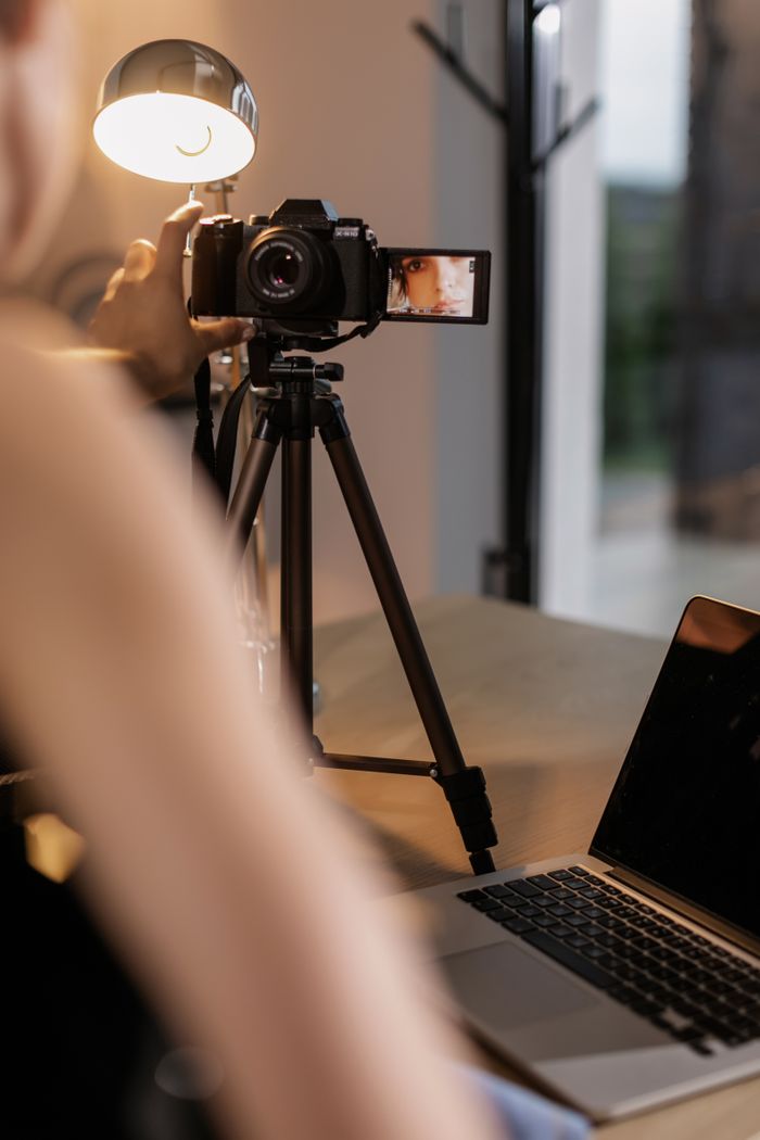 About A person sets up a DSLR camera on a tripod for vlogging indoors, illuminated by a lamp.